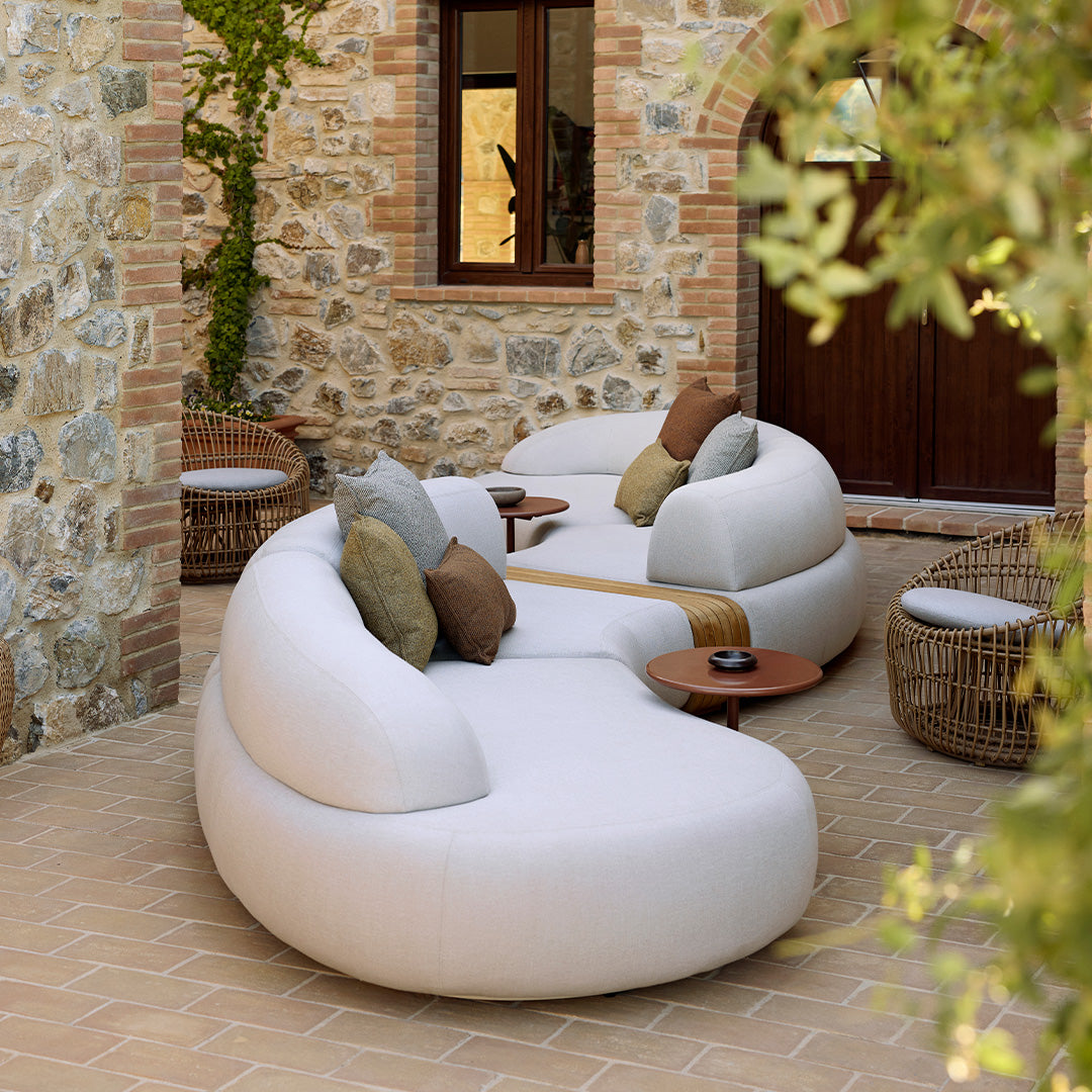Curved white outdoor sofas with textured neutral cushions, set against a rustic stone backdrop.