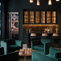 Luxurious emerald green velvet chairs with gold accents in a sleek, modern bar setting. Elegant dark tones dominate the space.