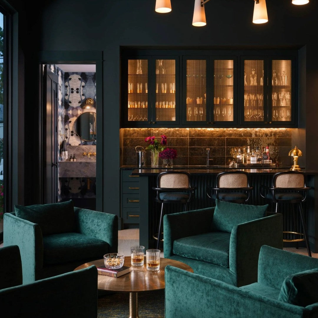 Emerald green velvet chairs against a dark wall, accented by gold lighting and bar cabinetry for a luxurious look.