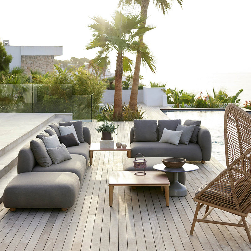 Stylish gray outdoor sofa set with soft cushions, complemented by natural wooden accents and palm tree backdrop.