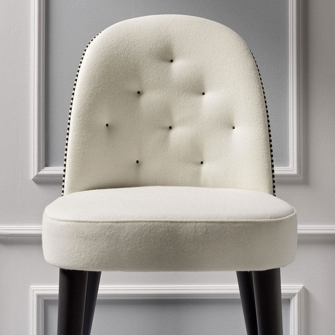 Cream upholstered chair with tufted design and black nailhead trim, featuring dark wooden legs.