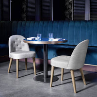 Gray tufted chairs with light wood legs beside a sleek table against a deep teal padded backdrop. Modern and stylish decor.