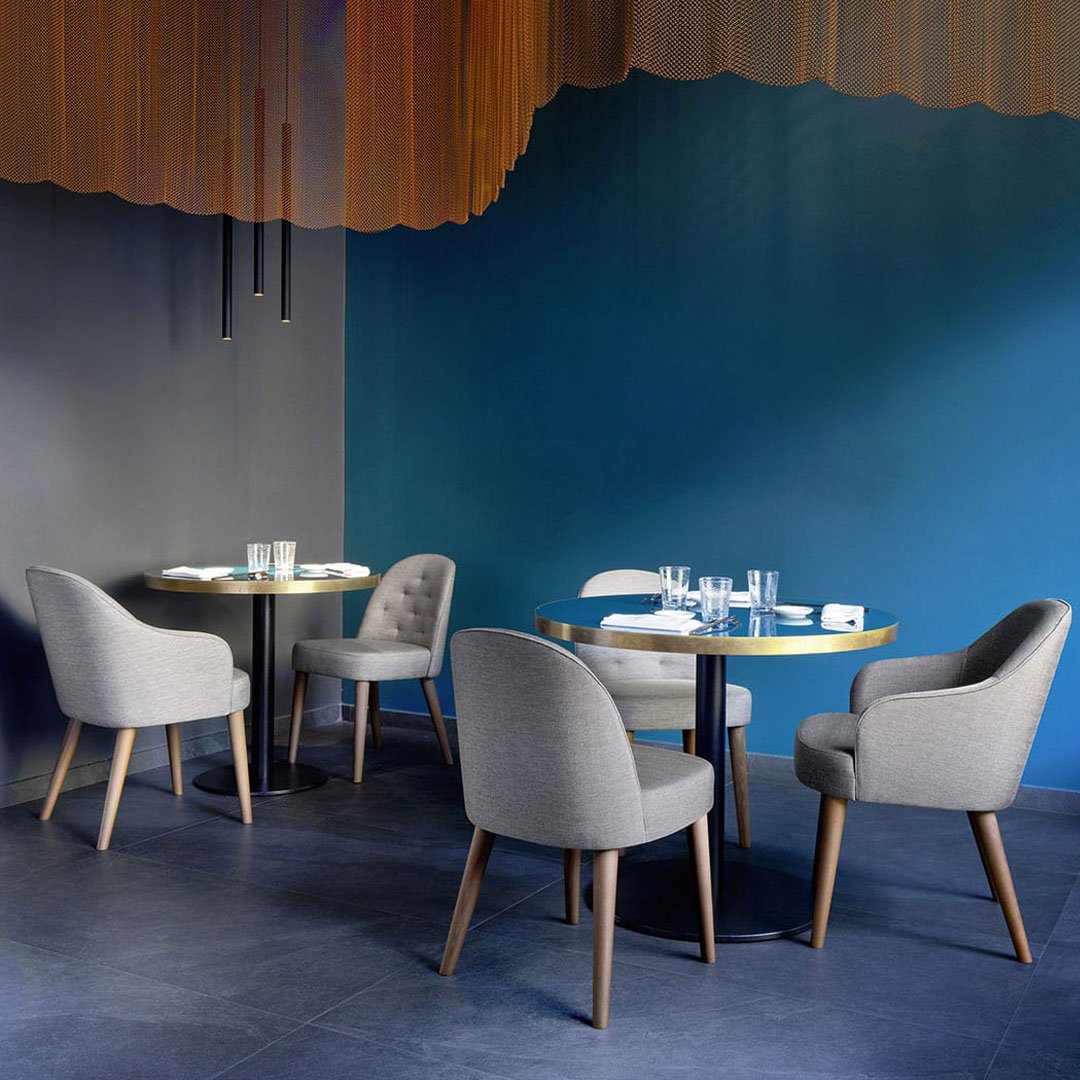 Stylish gray upholstered chairs and round tables against a bold blue wall and warm orange ceiling accents.