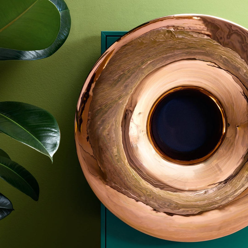 Copper bowl with shiny, marbled patterns, featuring deep blue center and set against vibrant green background.