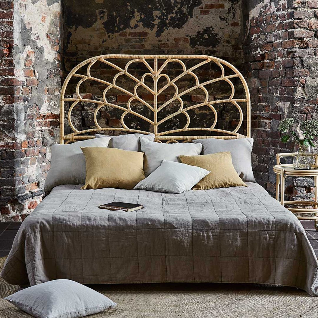 "Neutral-toned bedding with a textured quilt, surrounded by patterned cushions in soft blue and gold hues."