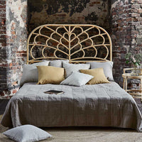 "Neutral-toned bedding with a textured quilt, surrounded by patterned cushions in soft blue and gold hues."