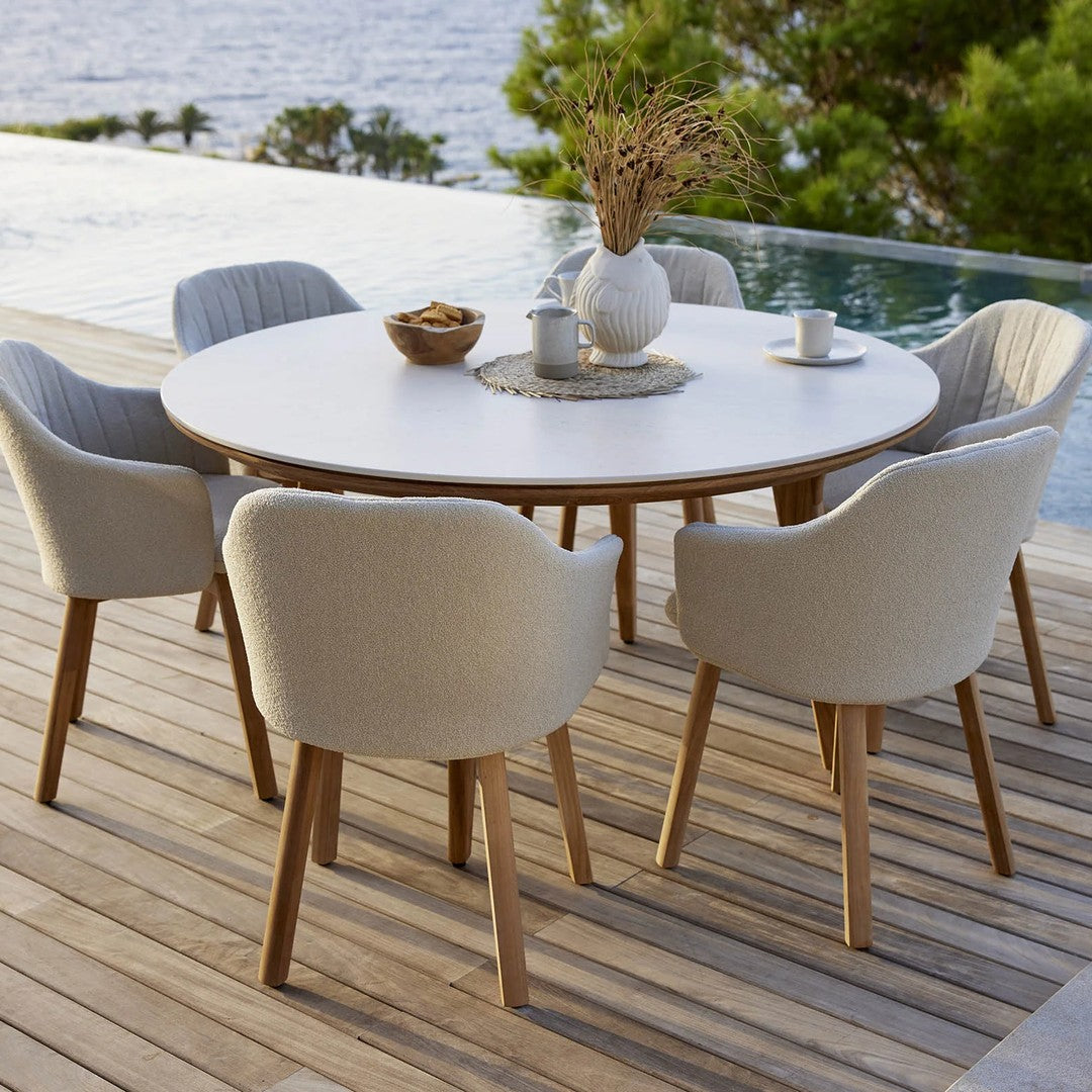Modern round dining table with white surface and natural wood accents, surrounded by soft beige textured chairs.