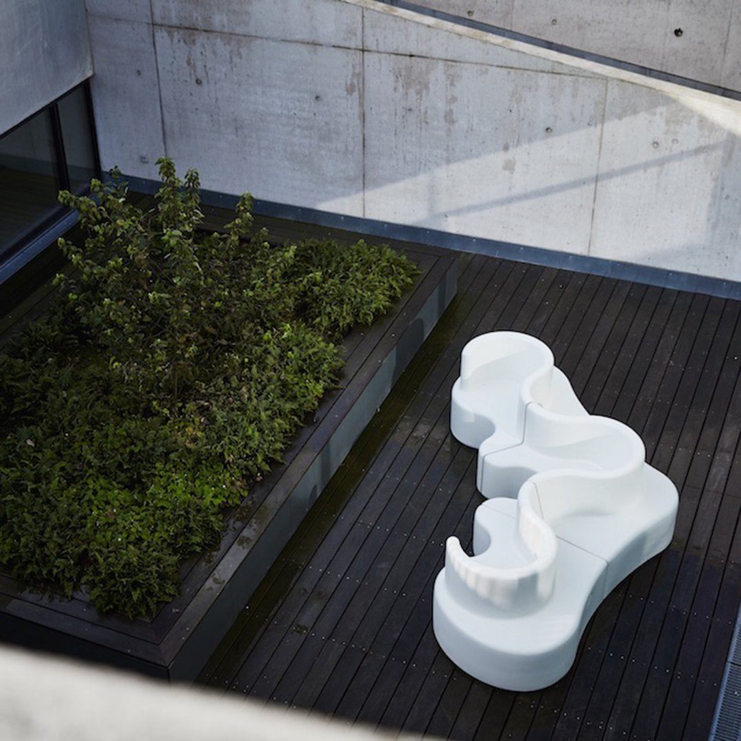 Elegant white sculptural seating positioned on dark wood deck surrounded by lush greenery. Modern geometric design.