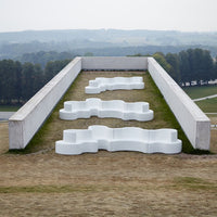 White wavy benches set on a grassy slope, surrounded by a neutral landscape under a soft gray sky.