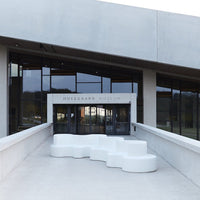 White, sculptural seating against a modern gray building; sleek lines and minimalist design for a contemporary aesthetic.
