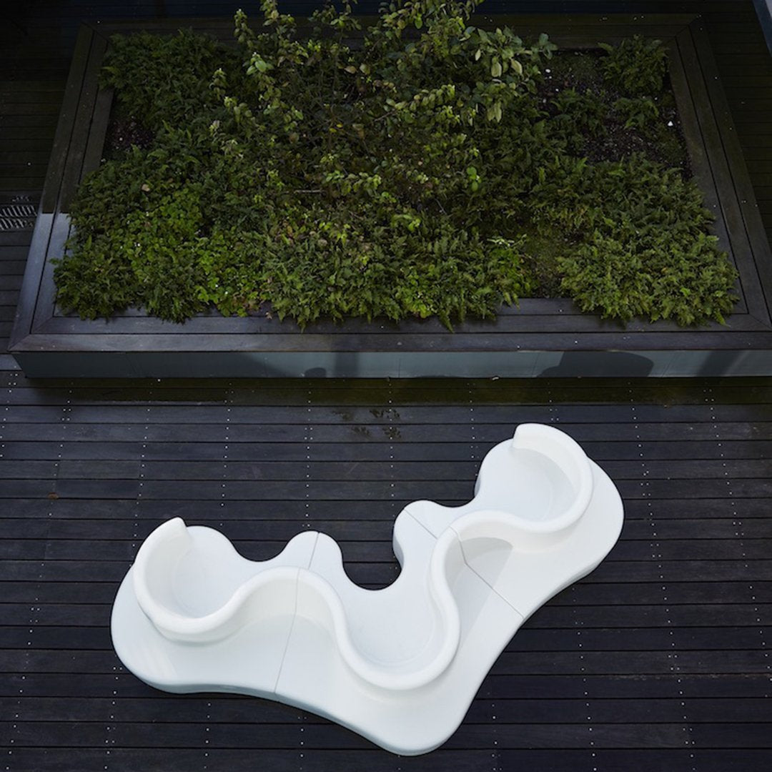 White abstract wavy design on dark wooden surface, surrounded by lush green foliage. 