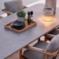 Gray stone table with wooden accents, complemented by dark plates and soft gray cushions. Modern, rustic elegance.