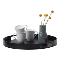 Black round tray with white textured cups and a green vase featuring yellow flower stems.