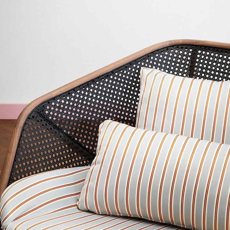 Striped cushions in gray, white, and orange on a wooden frame with a black caning pattern. Modern decorative accent.