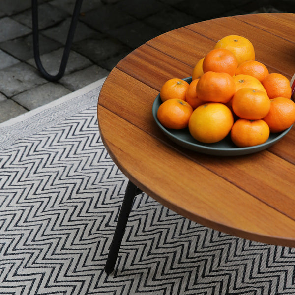 Wooden round table with oranges, set on a black and white herringbone patterned rug. Warm earthy tones.