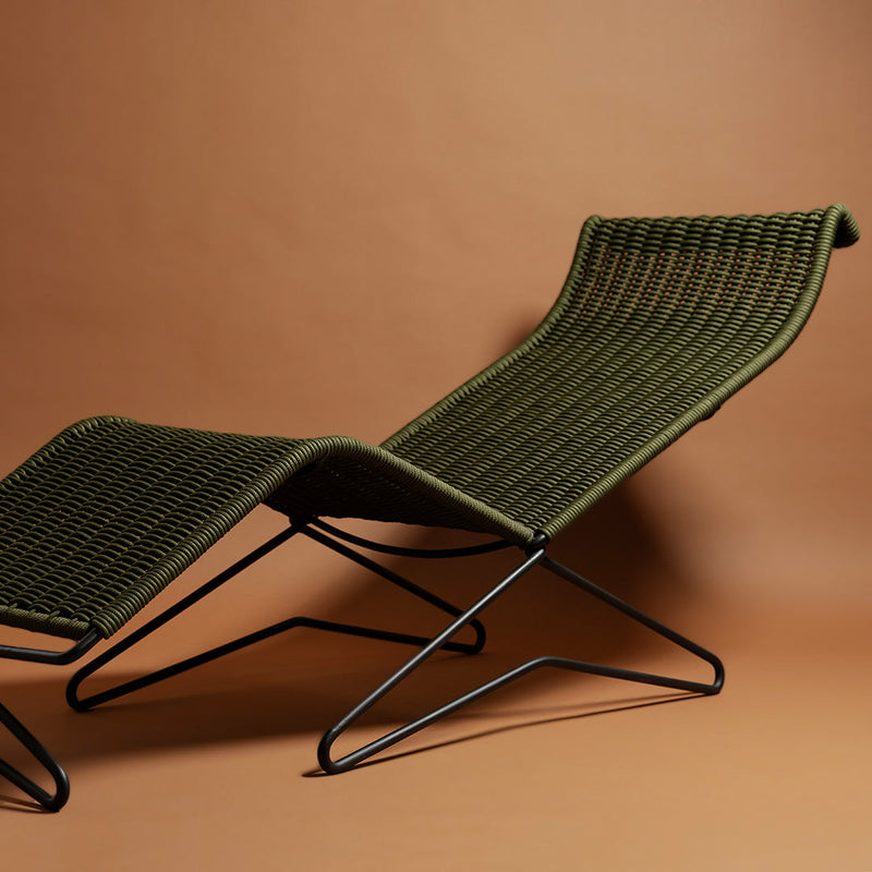 Green woven lounge chair with sleek black metal frame against a warm brown background. Stylish and modern design.