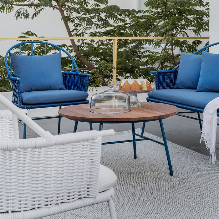 Blue cushioned chairs with woven white bases on a gray surface, complemented by a round wooden table.