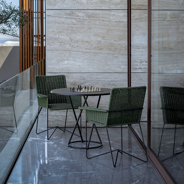 Green woven chairs with black metal frames around a circular black table on a sleek, polished floor.