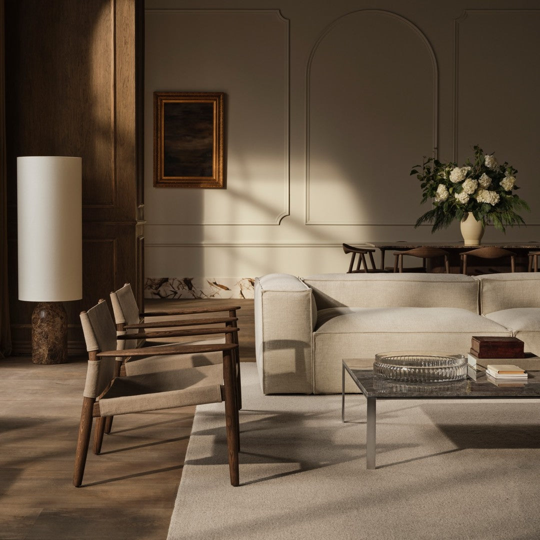 "Neutral-toned living room featuring beige sofa, wooden chairs, and a soft grey rug with subtle patterns."