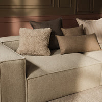 Beige textured sofa with a mix of brown and cream decorative pillows in various patterns, enhancing the cozy aesthetic.