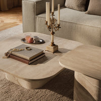 Light beige wooden coffee table with smooth curves, placed on a soft beige rug, surrounded by neutral-toned decor.