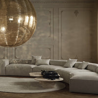 Curved beige sofa with textured pillows, round beige rug, and a shiny gold disco ball backdrop against soft beige walls.