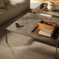 Gray marble coffee table with sleek lines, soft shadows, and natural wood accents on a light beige carpet.