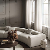 Curved beige sofa with light gray pillows, set against soft cream walls and sheer curtains, evoking modern elegance.