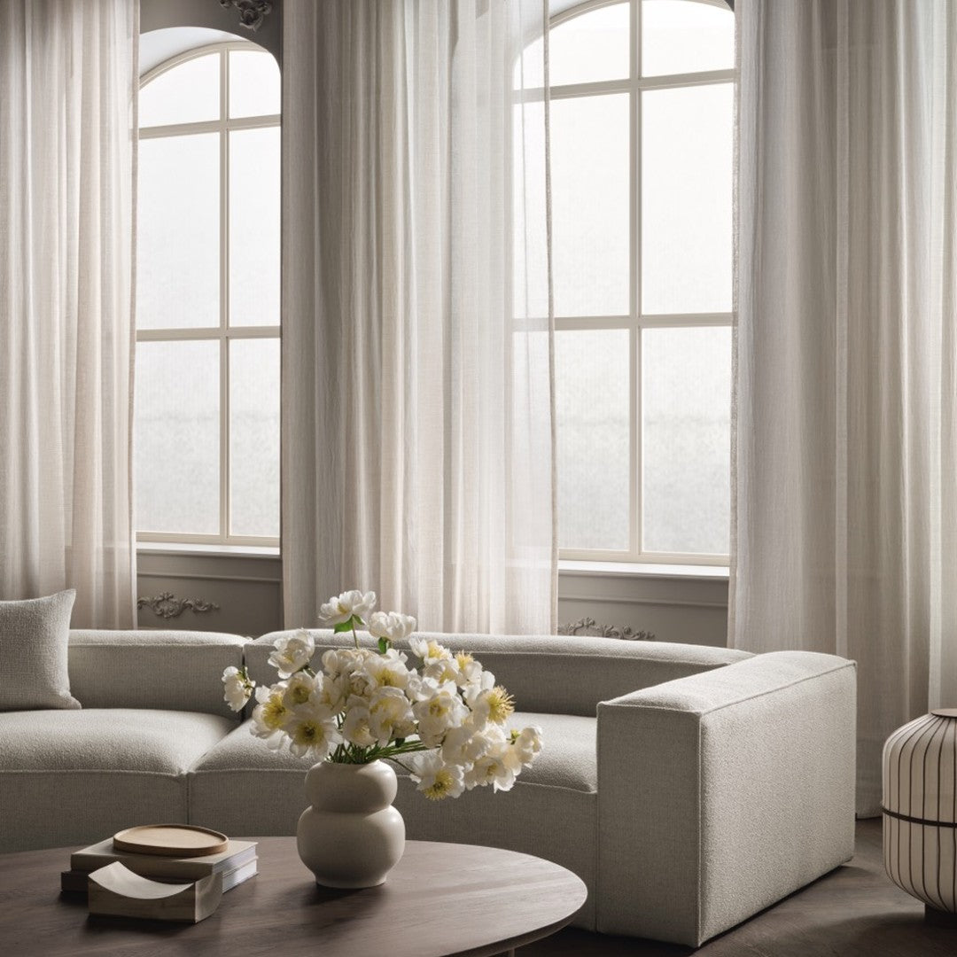 Light beige curtains, soft gray sofa, and white floral arrangement create a serene, neutral palette in a modern living space.
