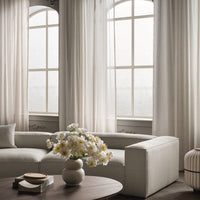 Light beige curtains, soft gray sofa, and white floral arrangement create a serene, neutral palette in a modern living space.