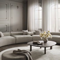 "Neutral beige sofa with gray walls and soft white curtains, accented by a round wooden table and patterned rug."
