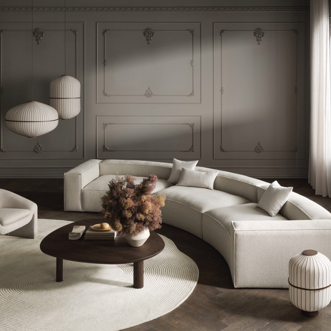 Curved cream sofa with subtle textures, dark wood table, and soft beige wall featuring elegant molding details.