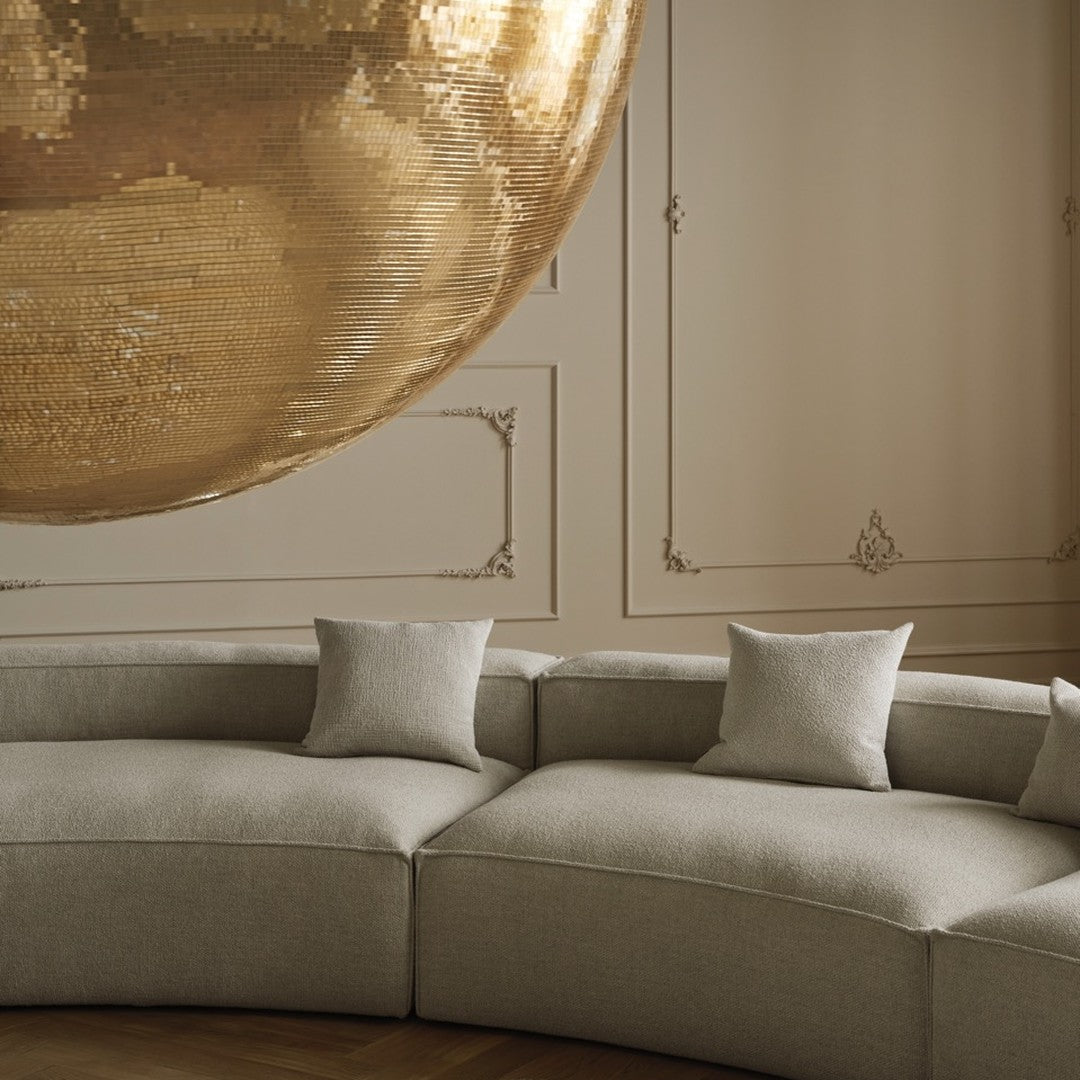Curved beige sofa with soft textured cushions, set against a neutral wall and glittering gold disco ball above.
