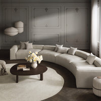 Curved beige sofa with light gray walls, white floral centerpiece, dark wood table, and textured cream area rug.