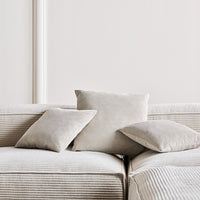 Neutral beige cushions with varying textures on a soft striped sofa in a modern setting.