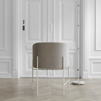 Gray upholstered chair with minimalist white metal legs, set against a sleek, light wood floor and white paneling.