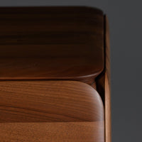 Close-up of smooth, rich walnut wood finish with subtle curves, highlighting warm brown tones and natural grain patterns.