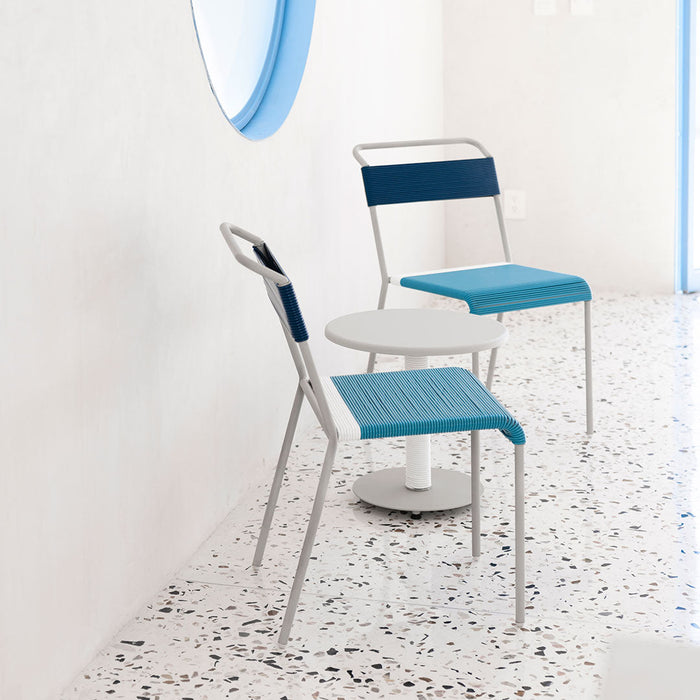 Set of two modern chairs with blue and gray features, paired with a round table on a speckled terrazzo floor.