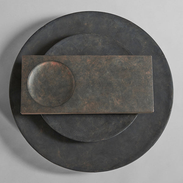 Dark, textured plates in varying circular and rectangular shapes showcasing an earthy, industrial finish.