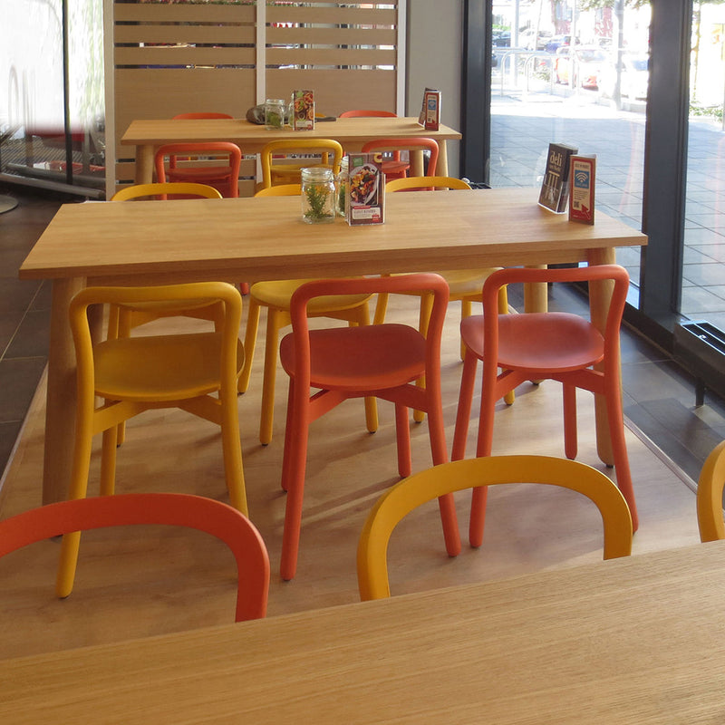 Vibrant yellow and orange chairs around a light wood table in a modern dining space. Bright and cheerful decor.