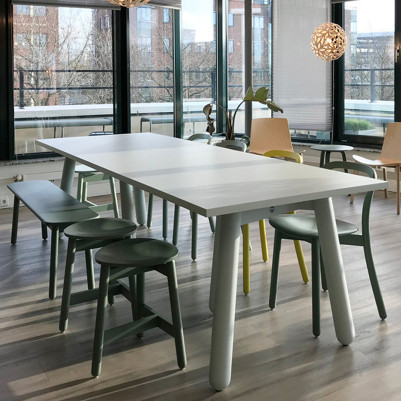 Modern dining table featuring a white top, light gray legs, and green and yellow accent chairs.