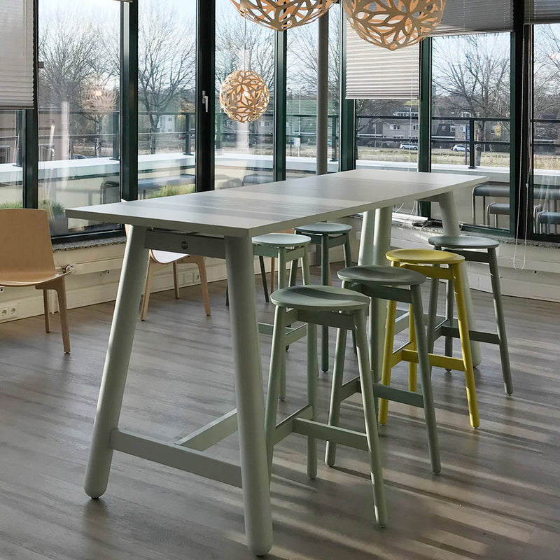 Modern bar table with a white top and pastel green, blue, and yellow stools, surrounded by natural light.
