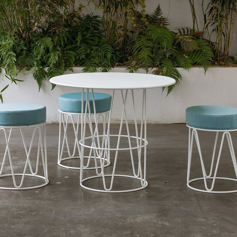 White round table with four sky blue stools, featuring sleek wire bases and a modern design against a green backdrop.