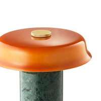 Glossy orange top with a gold knob resting on a textured green base, creating a modern design contrast.