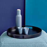 Blue and black dinnerware set featuring a matte tray, round base, and sleek bottles and cups against a textured backdrop.