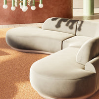 Curved beige sofa on textured orange rug, featuring soft lines and a minimalist design for modern interiors.