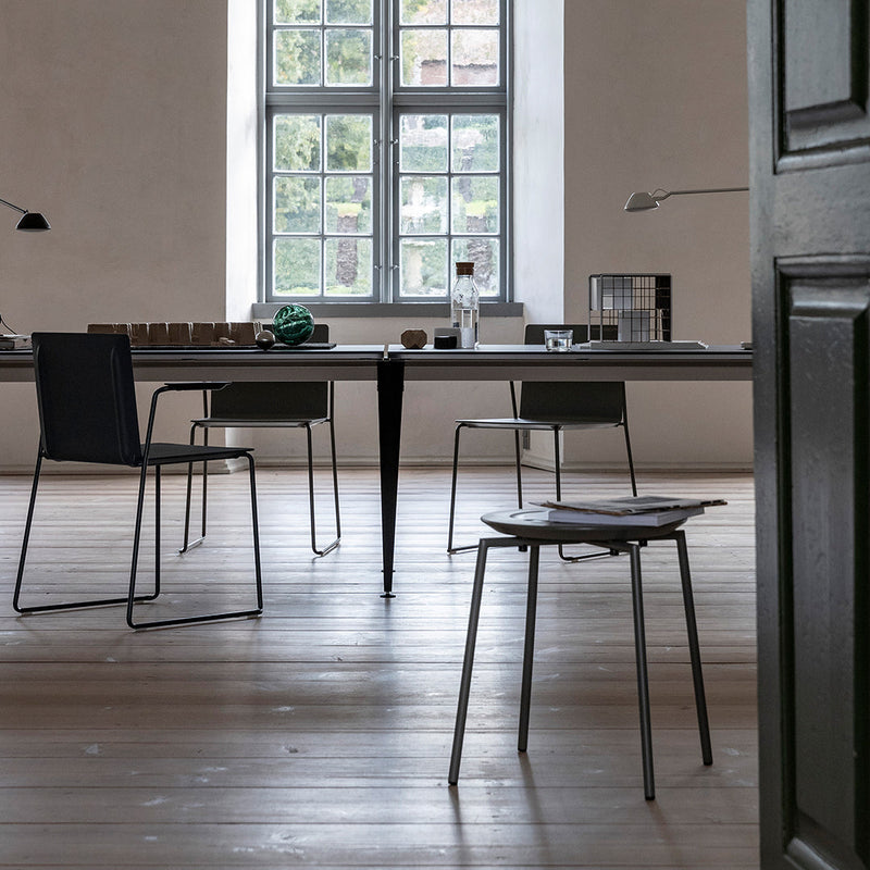 Modern dining area with grey chairs and a sleek black table, illuminated by natural light through large windows.