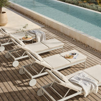 Neutral beige lounge chairs with subtle textures, set on a wooden deck beside a serene blue pool.