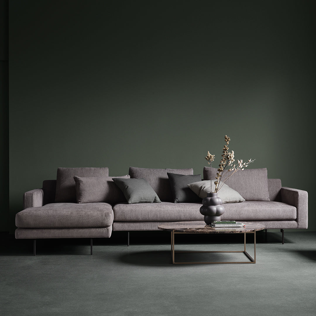 Gray sectional sofa with soft, muted pillows against a dark green wall and a sleek coffee table.