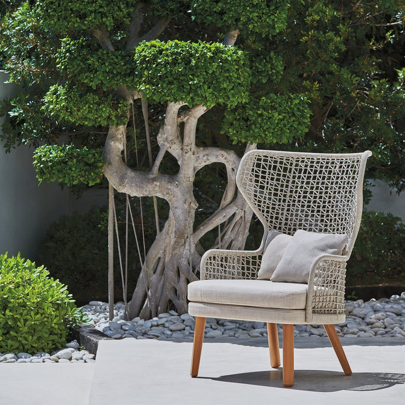 Beige woven chair with a unique pattern, complemented by natural wood legs against a green outdoor backdrop.